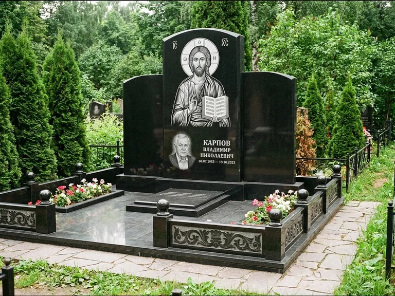 Памятник с гравировкой иконы: широкая панорамная стела с золочёным нимбом — гравировка образа Матроны Московской, цветник с белыми хризантемами, работа «Мельникова» в Белгороде