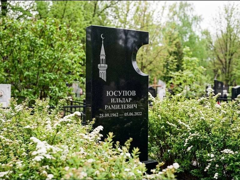 Мусульманский памятник с гравировкой мечети: стела с боковым вырезом в форме полумесяца — гравировка минарета с полумесяцем, низкие кусты спиреи в цвету, работа «Юсупов» в Белгороде
